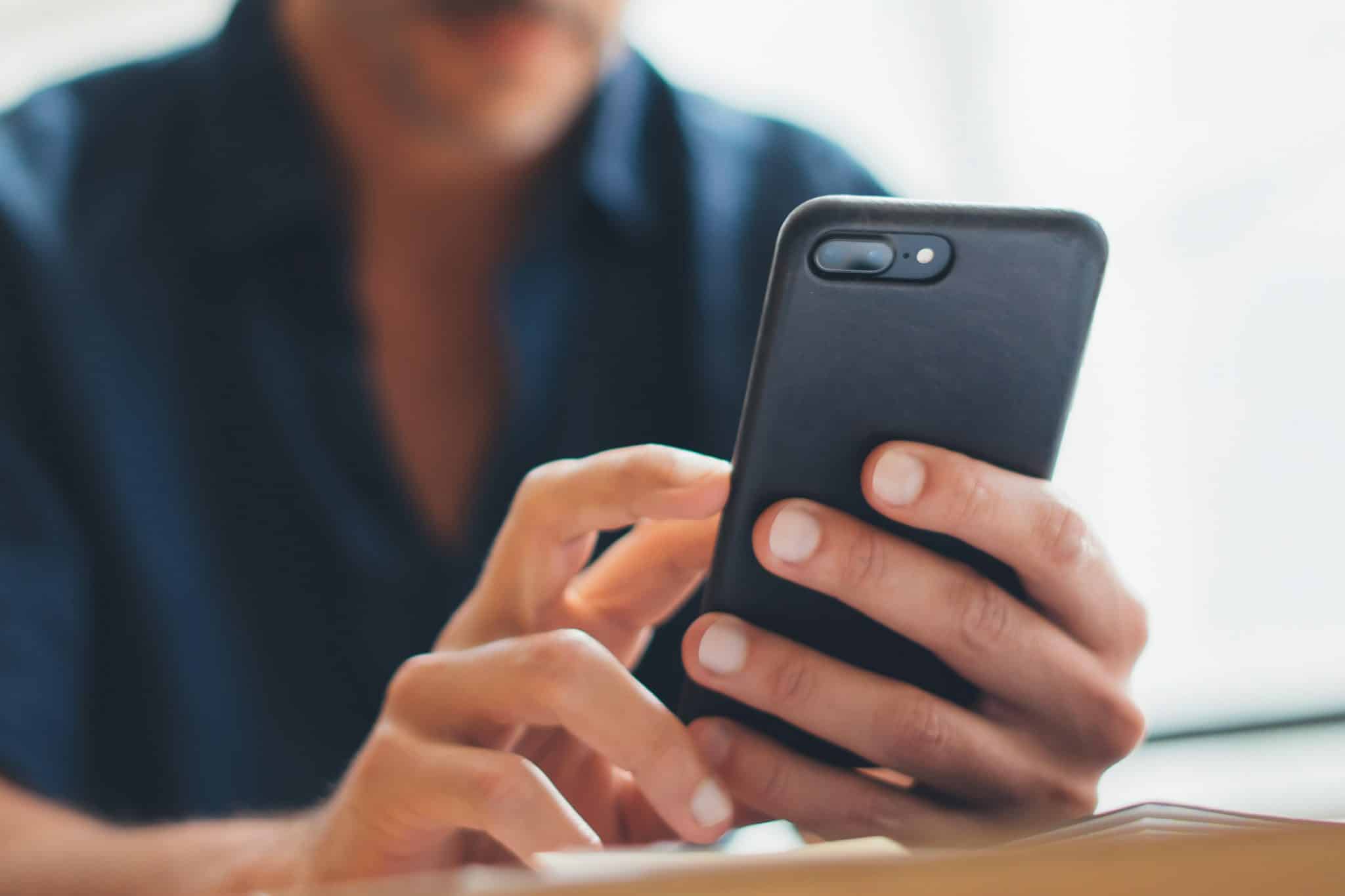 Uomo seduto a un tavolo che usa uno smartphone per effettuare il check-in online - tassa di soggiorno